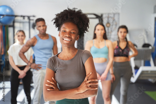 Confident woman smiling while posing in front of a group of sporty people in the gym. Sports concept.