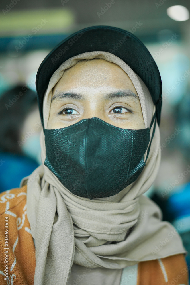 Smiling young asian woman in hijab wearing mask and hat sitting in waiting room Smiling young asian woman in hijab wearing mask and hat sitting in waiting room