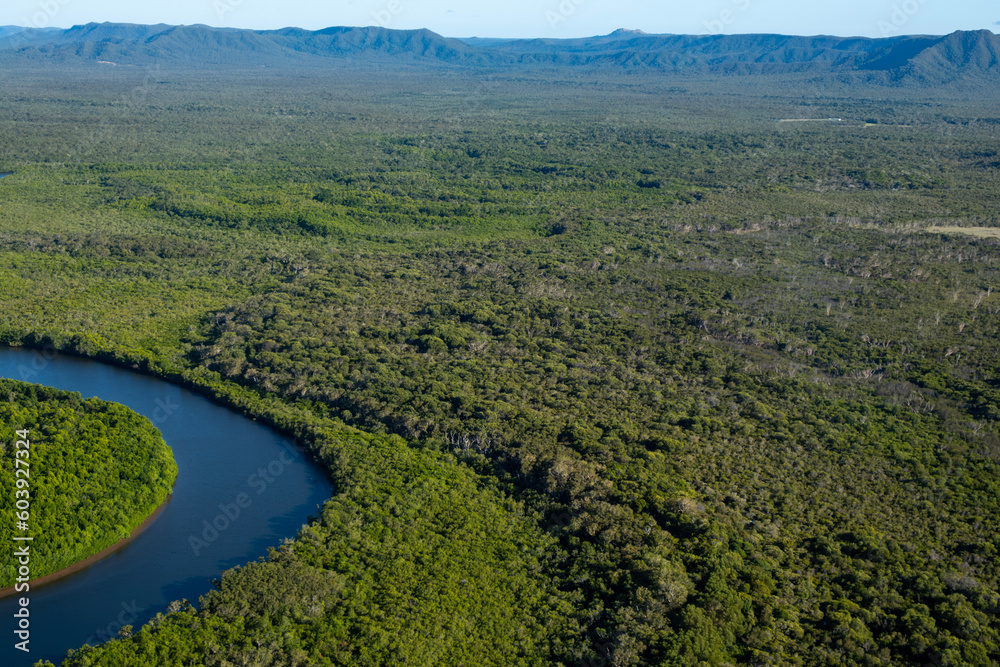 Aerial view of the wild crocodile country on a flight to the tip of Australia, Queensland. There is a winding river with sweeping plain and hills in the background with horizon and sky.