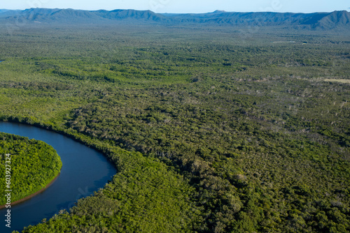 Aerial view of the wild crocodile country on a flight to the tip of Australia, Queensland. There is a winding river with sweeping plain and hills in the background with horizon and sky.