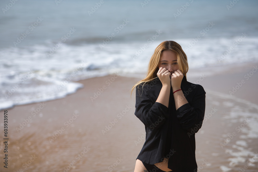 Young woman, blonde and beautiful, wearing a bikini and black shirt, clutching the collar of the shirt to cover her face, loving herself. Concept purity, virginity, protection. Young woman, blonde and beautiful, wearing a bikini and black shirt, clutching the collar of the shirt to cover her face, loving herself. Concept purity, virginity, protection.