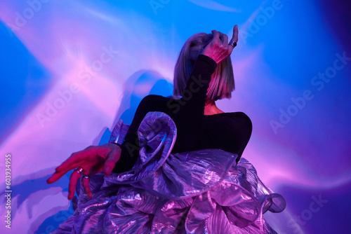 Horizontal medium studio shot of unrecognizable senior Caucasian woman with blond hair wearing unusual outfit posing on camera in neon light  photo