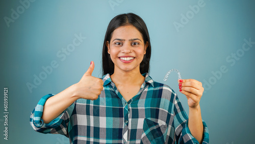 Young Asian Indian woman holding removable invisible aligner, also known as invisalign or  clear aligner