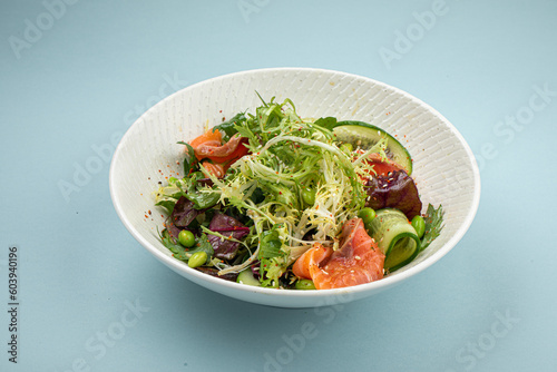 Portion of fresh gourmet salad with salmon on blue background