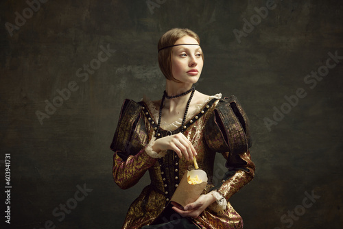 Portrait of young beautiful woman in vintage costume, eating fries against dark green background. Fast food lover. Concept of history, renaissance art, comparison of eras, health and modern food