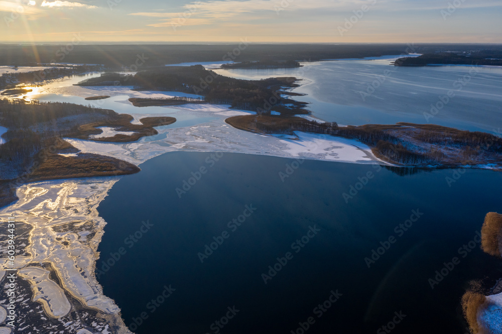 Beautiful winter landscape - drone aerial photo sunset time - frozen Wigry lake, forest and sun reflections in water and ice