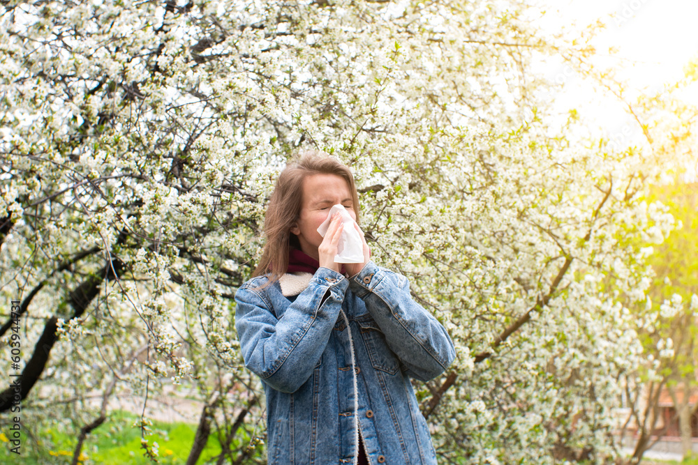 Woman sneezing into a handkerchief near a tree full of blossoms. She is suffering from seasonal spring allergy. Woman sneezing into a handkerchief near a tree full of blossoms. She is suffering from seasonal spring allergy.