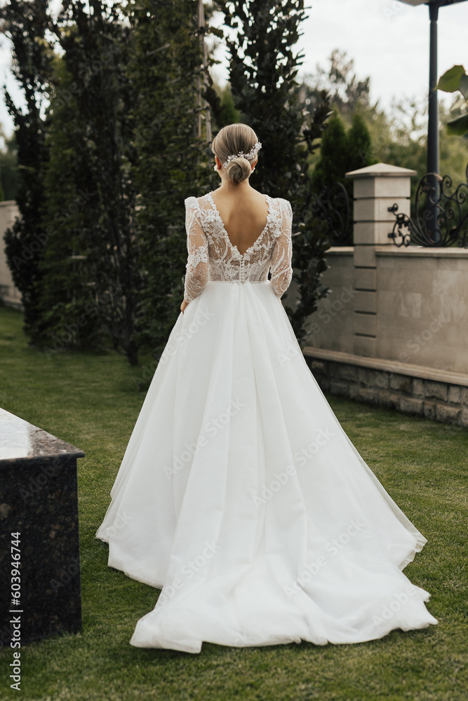 Bride in a white wedding long dress walks in the garden, back view. Wedding concept.	