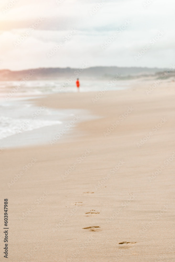 Beach travel - woman in a red dress walking along the beach leaves footprints in the sand.