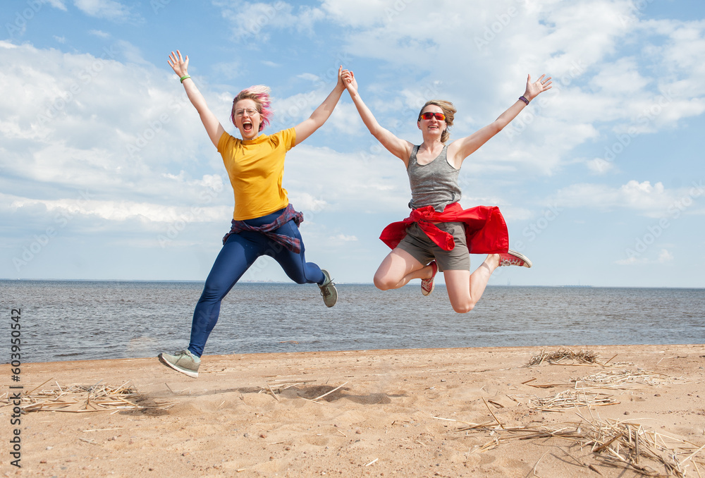 Two cheerful young women having fun and jumping on the sand