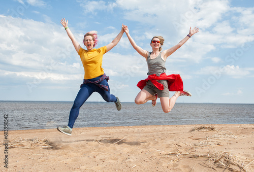 Two cheerful young women having fun and jumping on the sand