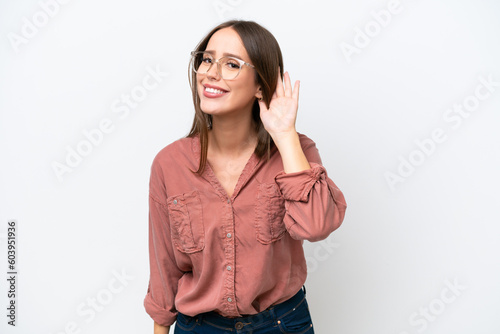 Young pretty caucasian woman isolated on white background listening to something by putting hand on the ear