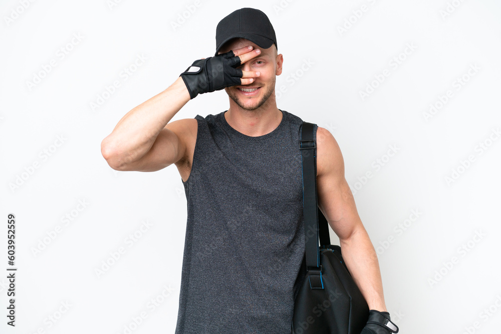 Young blonde sport caucasian man with sport bag over isolated white background covering eyes by hands and smiling Young blonde sport caucasian man with sport bag over isolated white background covering eyes by hands and smiling