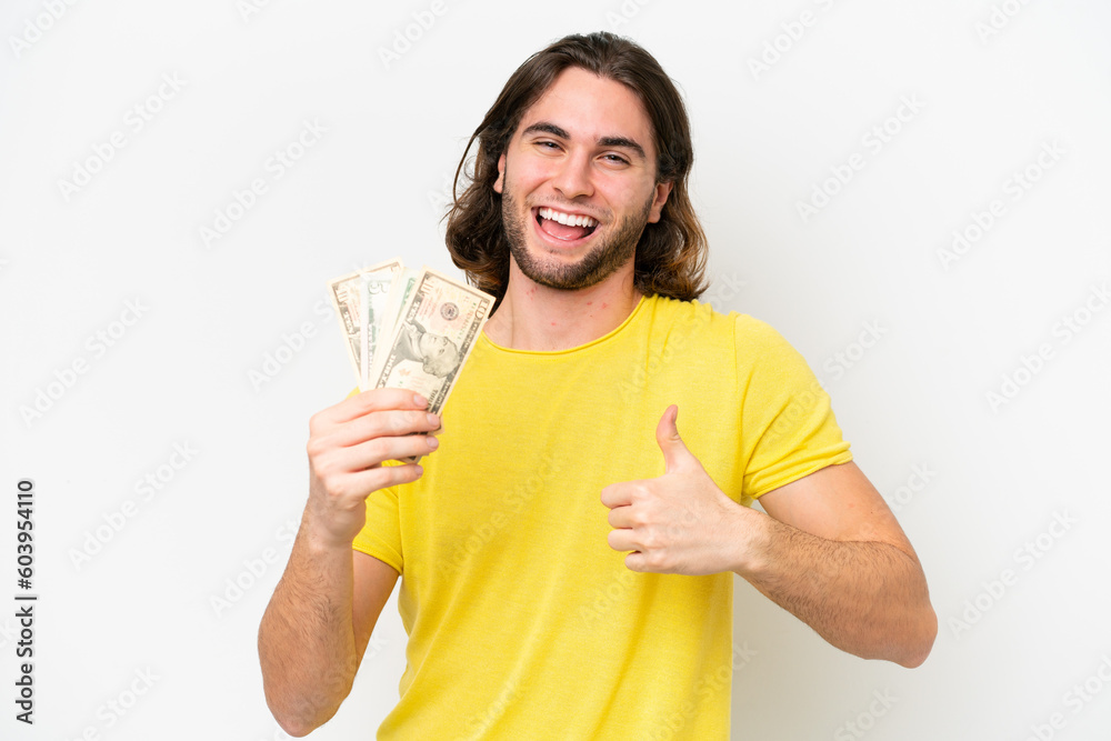 Young handsome man taking a lot of money isolated on white background with thumbs up because something good has happened Young handsome man taking a lot of money isolated on white background with thumbs up because something good has happened
