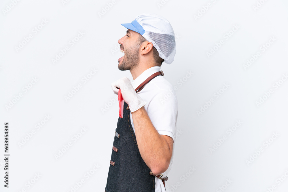 Butcher caucasian man wearing an apron and serving fresh cut meat over isolated white background laughing in lateral position Butcher caucasian man wearing an apron and serving fresh cut meat over isolated white background laughing in lateral position