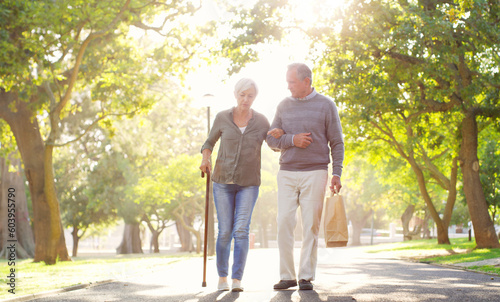 Senior couple, cane and walking outdoor at a park with a love, care and support for health and wellness. A elderly man and woman in nature for a walk, quality time and healthy marriage or retirement