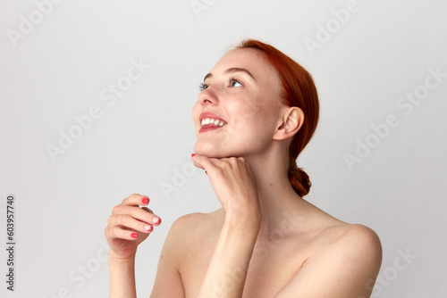 Close up shot of happy, adorable girl with perfect skin and red hair doing neck massage over white studio background. Beauty, spa, cosmetology photo