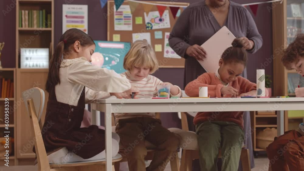 Cropped shot of unrecognizable Black female teacher working with multiethnic elementary age children drawing at table in modern classroom