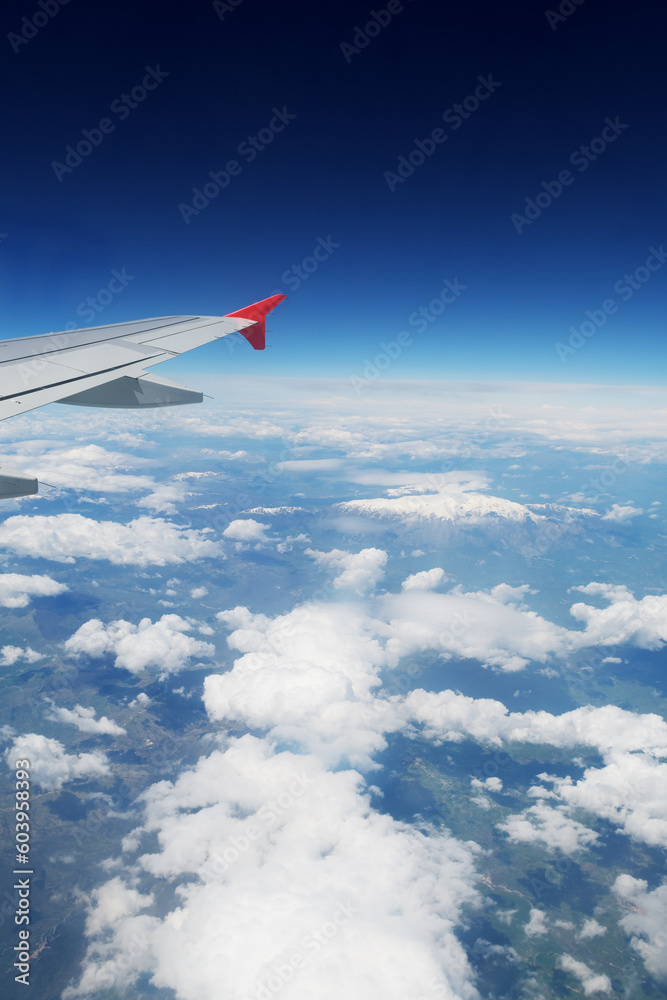 Fototapeta premium A view through an airplane window. Visible wing, clouds over land and space