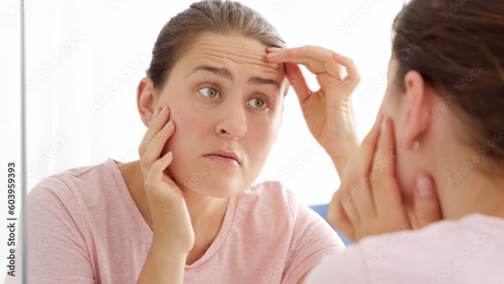 Brunette woman looking at her reflection in mirror and finding wrinkles on forehead Brunette woman looking at her reflection in mirror and finding wrinkles on forehead