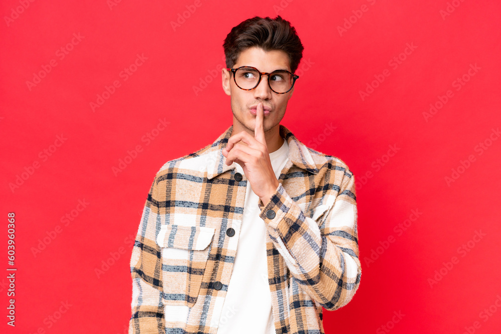 Young caucasian handsome man isolated on red background showing a sign of silence gesture putting finger in mouth Young caucasian handsome man isolated on red background showing a sign of silence gesture putting finger in mouth