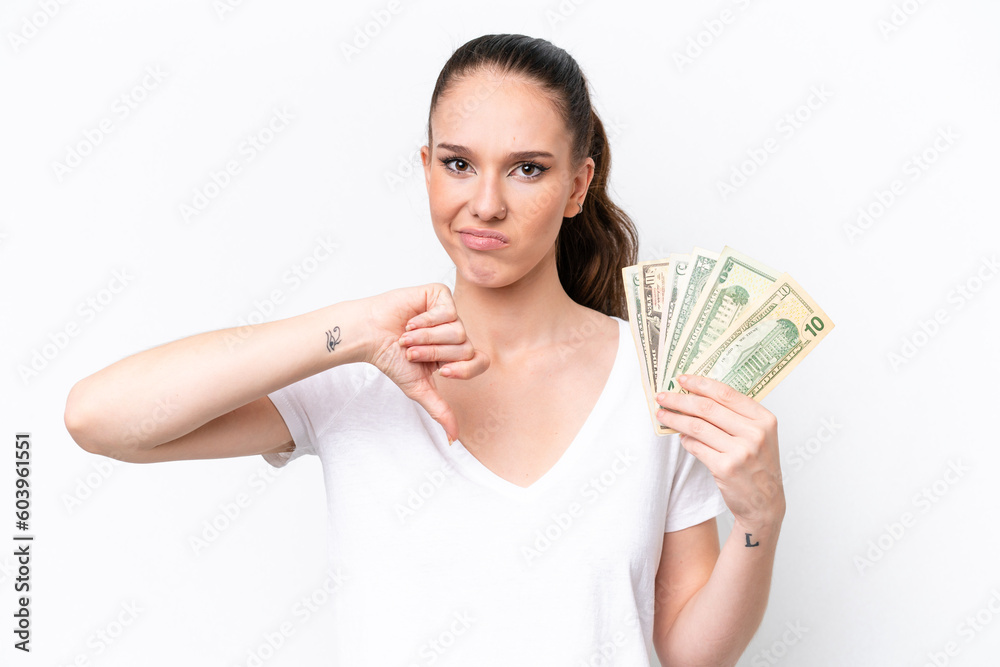 Young caucasian woman taking a lot of money isolated on white background showing thumb down with negative expression Young caucasian woman taking a lot of money isolated on white background showing thumb down with negative expression