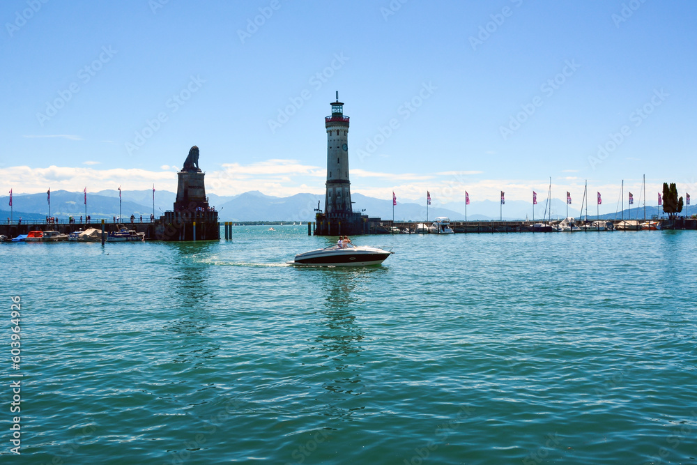 There is a lighthouse on the sea pier with boats. A motor boat floats on the turquoise waves.