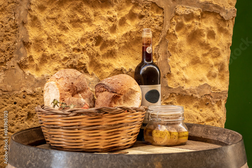 Bottle of wine, artisan bread in wicker basket and marinated cheese in a jar on a wooden barrel. Traditional  food products of Malta. 
