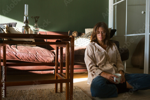 Woman sitting on floor by sofa with coffee cup photo