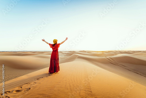 Fototapeta Woman wearing hijab walking in the desert sand dunes at sunset - Happy traveler