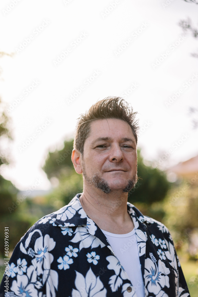Portrait of a mature man with sideburns dressed in Hawaiian shirt in a garden at sunset. Men's fashion and beauty in travel and vacation. Portrait of a mature man with sideburns dressed in Hawaiian shirt in a garden at sunset. Men's fashion and beauty in travel and vacation.