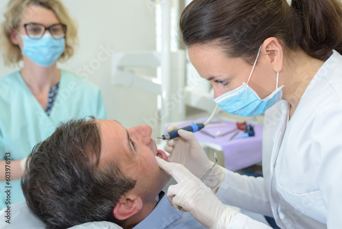 dentist examining a male patient with tools in clinic
