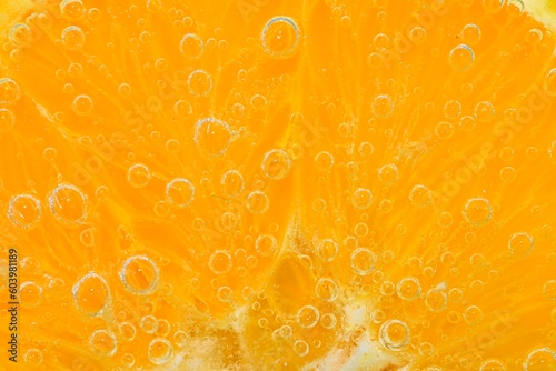 Slice of orange fruit in sparkling water. Orange fruit slice covered by bubbles in carbonated water. Orange fruit slice in water with bubbles. Close-up, macro horizontal image.