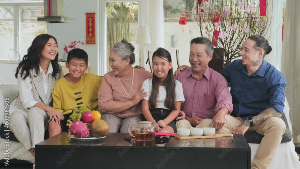 Happy multigenerational Asian family sitting on couch in living room decorated for Tet, chatting and smiling together on camera while gathering for celebration Happy multigenerational Asian family sitting on couch in living room decorated for Tet, chatting and smiling together on camera while gathering for celebration