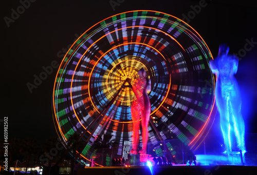 Ferris wheel at amusement theme park in the evening time. Batumi Boulevard. Photo is taken with a long exposure and has motion blur. “Statue of Love”, Ali & Nino Statue. night scene.