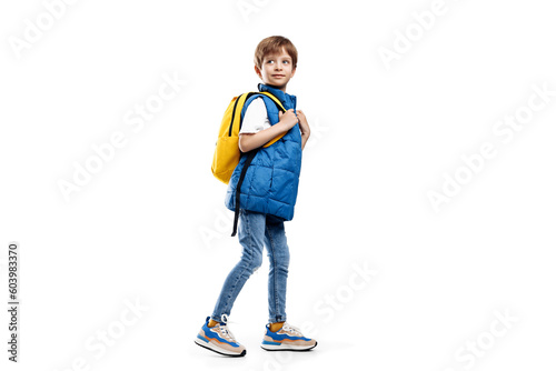 Full lengh image of a little boy with backpack walking over white background. Back to School. Looking away. photo