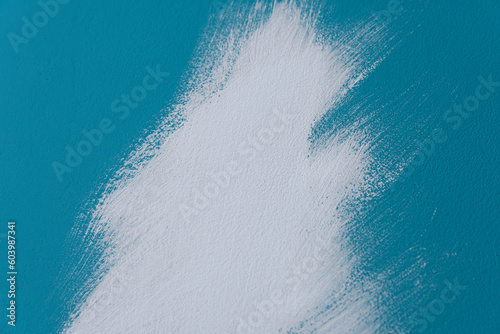 Close up of smear of white paint with a paint brush on a blue wall. Creative background