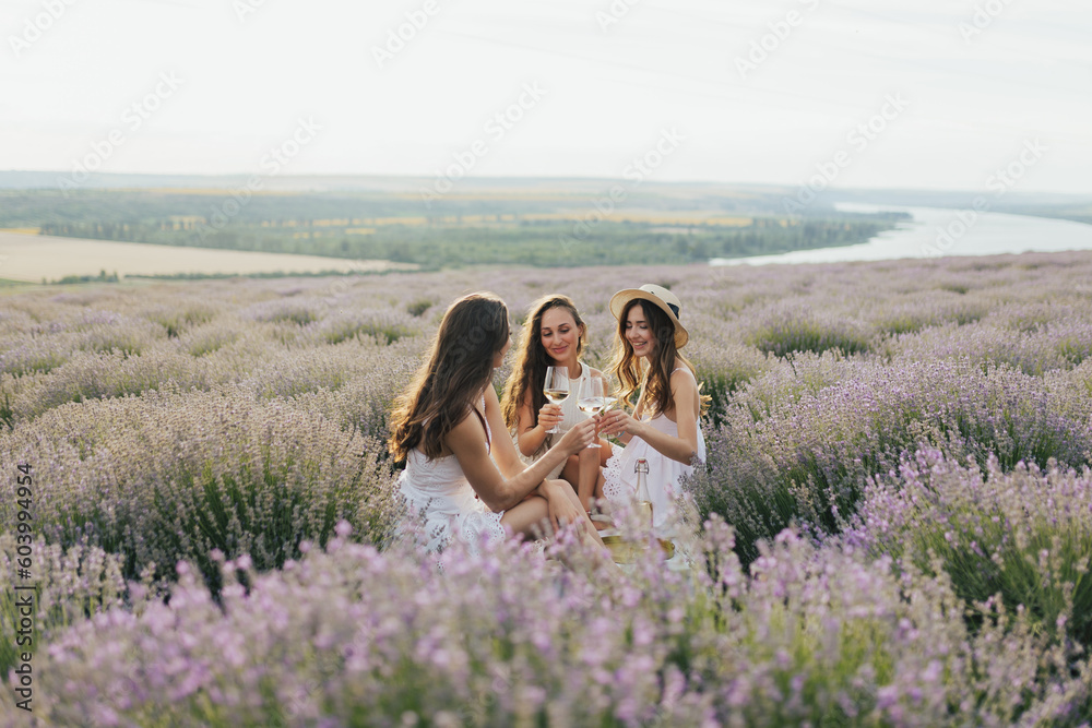 Group of friends having fun on picnic on the lavender field, sitting and drinking wine.