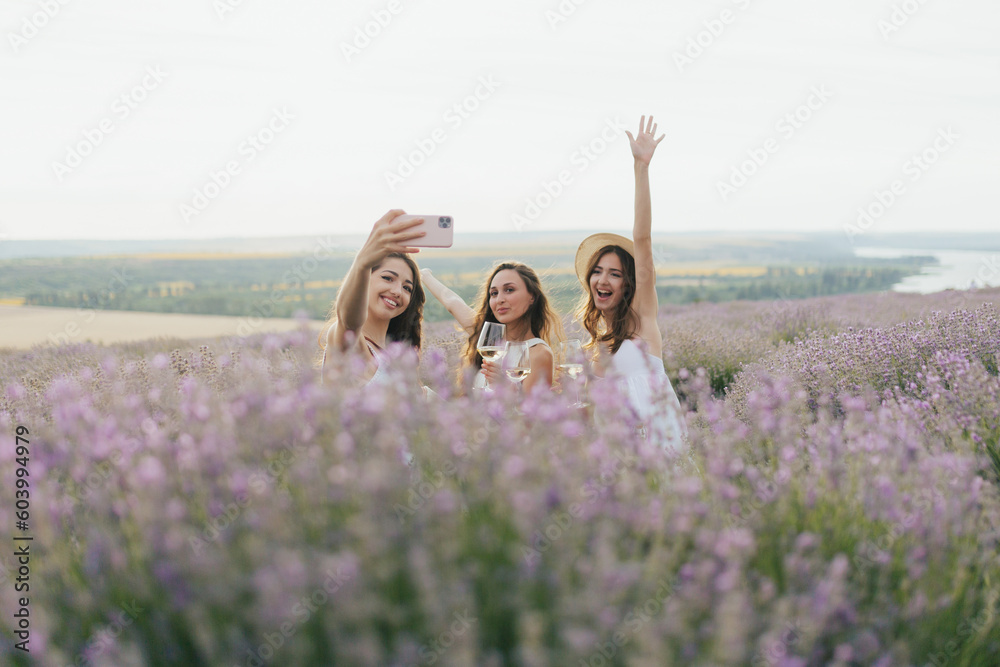 Group of friends doing summer picnic in nature. Happy people have fun, smiling and drinking white wine. Friends on summer day are sitting on the lavender field.