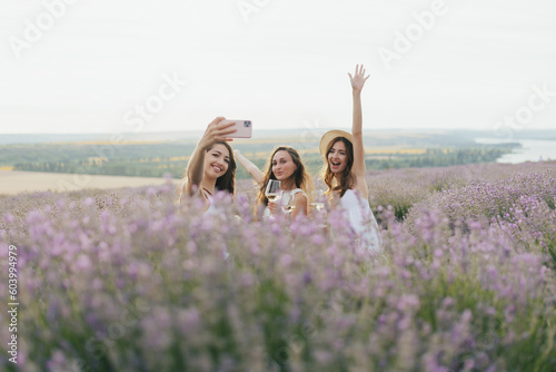 Obraz na płótnie Group of friends doing summer picnic in nature. Happy people have fun, smiling and drinking white wine. Friends on summer day are sitting on the lavender field. w salonie