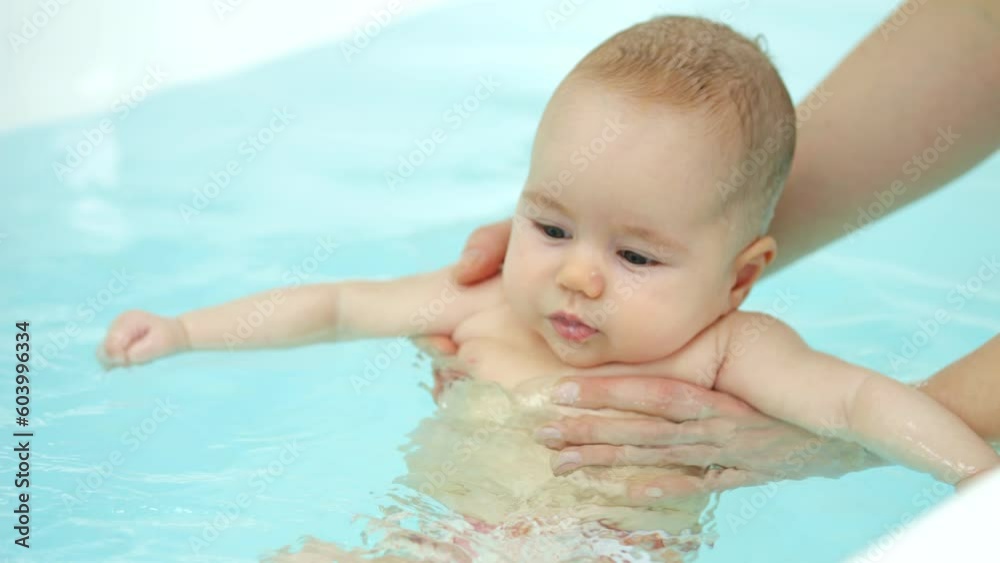 Swim teacher holds baby under arms and girl swings legs in bathtub. Newborn girl face expresses happiness and joy from swimming process Swim teacher holds baby under arms and girl swings legs in bathtub. Newborn girl face expresses happiness and joy from swimming process