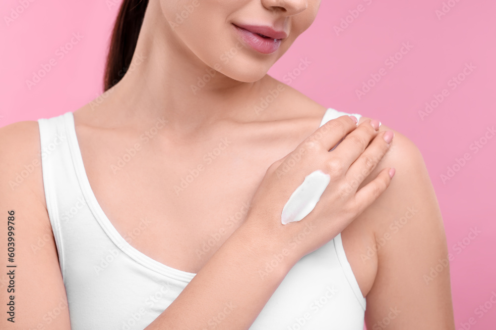 Woman with smear of body cream on her hand against pink background, closeup