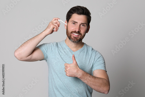 Man using ear spray and showing thumbs up on grey background