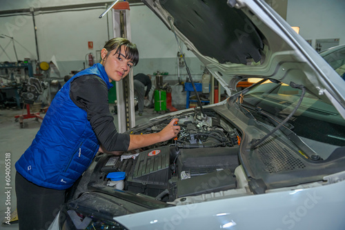 Young female mechanic, working on the repair of a car engine.