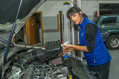 Young female mechanic, checking the air filter, of a car engine.