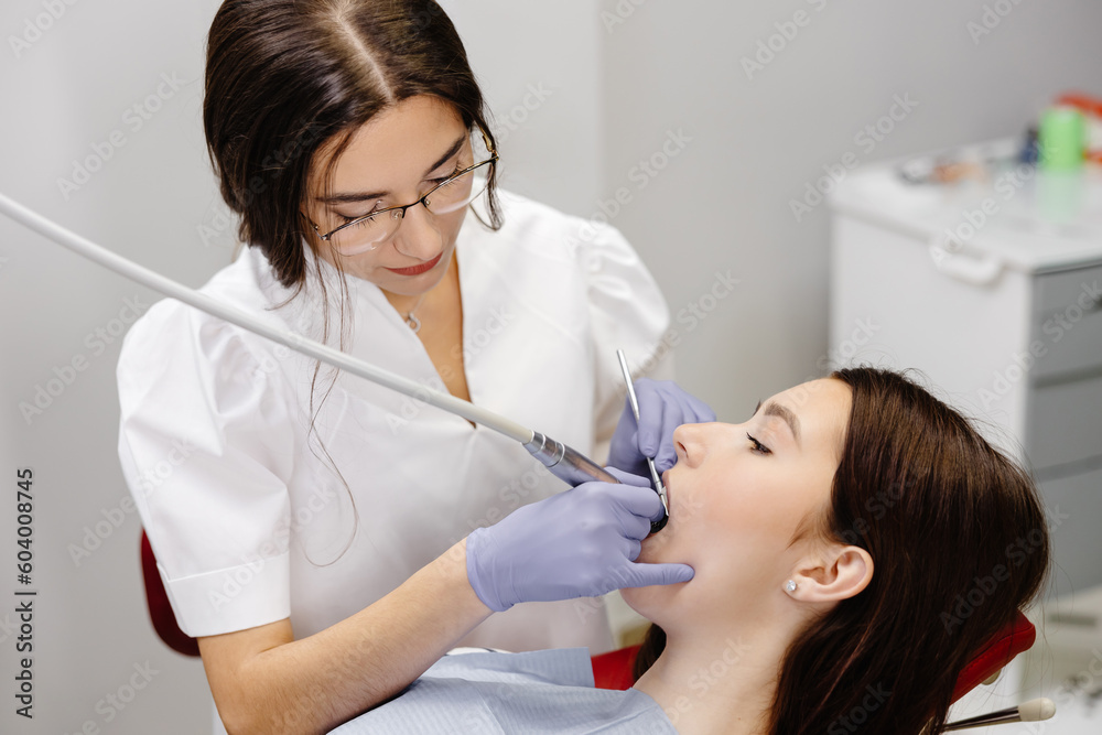 Teeth health concept. Attractive girl opening mouth under treatment at dental clinic and dentist woman doing treatment her teeth Teeth health concept. Attractive girl opening mouth under treatment at dental clinic and dentist woman doing treatment her teeth