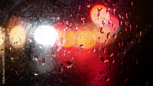Headlights and rear red lights of cars through the wet glass of a car. Beautiful multi-colored stains of light refraction through wet glass.