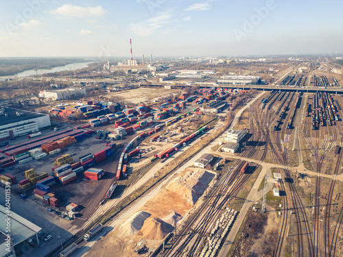 Cargo trains. Aerial view of colorful freight trains. Railway station. Wagons with goods on railroad. Heavy industry. Industrial scene with trains, city buildings and cloudy sky at sunset. Top view