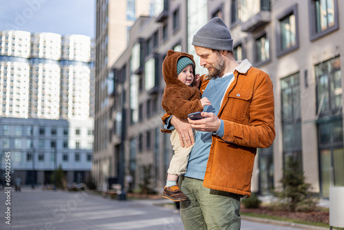 A man with a child on his back walks down the street, holding a phone 