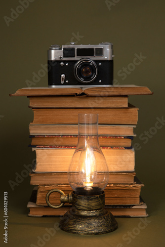 Old books, an old camera and a vintage style lamp with the light on.